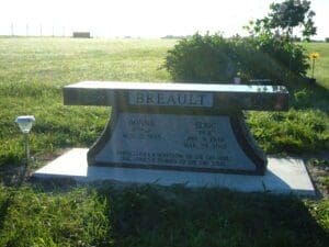 Sunlit granite memorial bench in grassy cemetery