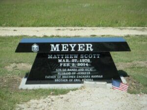 Black bench style gravestone with small American flag